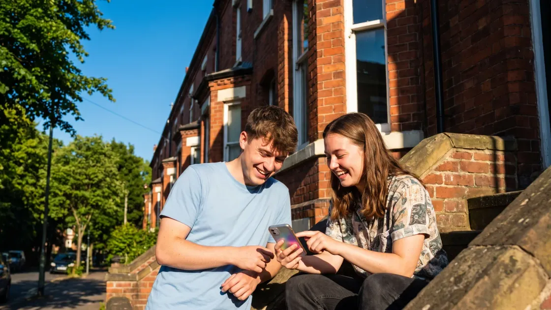 Two students sitting on the sunny front steps of their terraced house